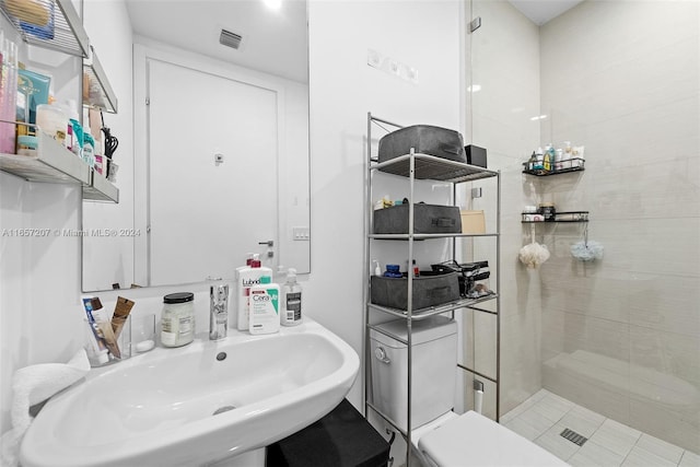 bathroom with toilet, a tile shower, and sink