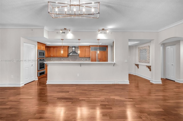 kitchen featuring ornamental molding, appliances with stainless steel finishes, hardwood / wood-style flooring, and wall chimney exhaust hood