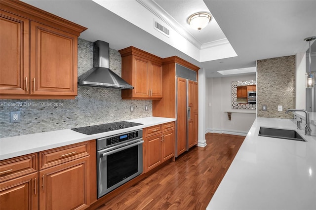 kitchen with built in appliances, sink, wall chimney exhaust hood, and tasteful backsplash