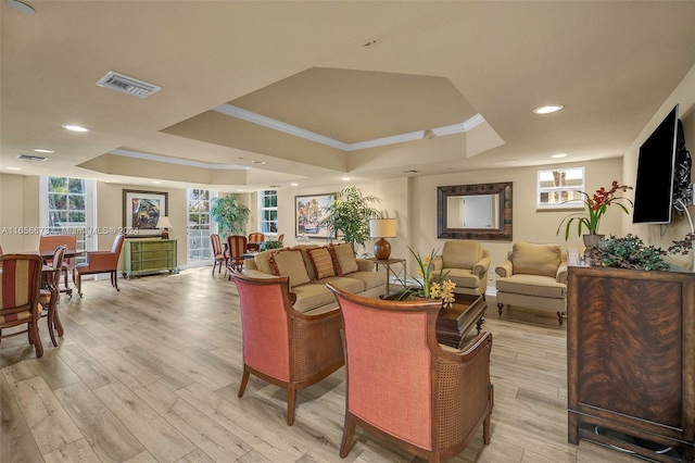 living room with light hardwood / wood-style flooring, ornamental molding, and a tray ceiling