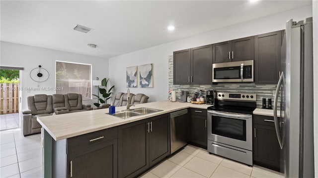 kitchen featuring appliances with stainless steel finishes, tasteful backsplash, kitchen peninsula, light tile patterned floors, and dark brown cabinetry