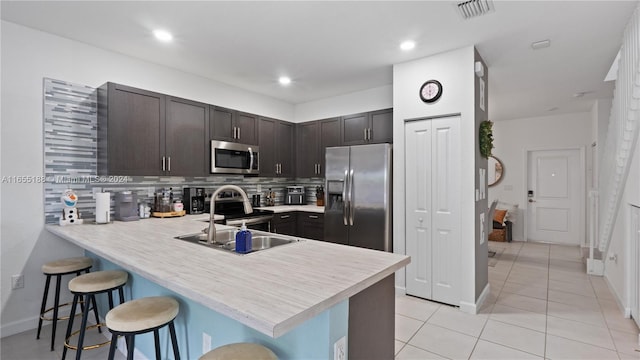 kitchen featuring dark brown cabinetry, kitchen peninsula, stainless steel appliances, a kitchen bar, and decorative backsplash