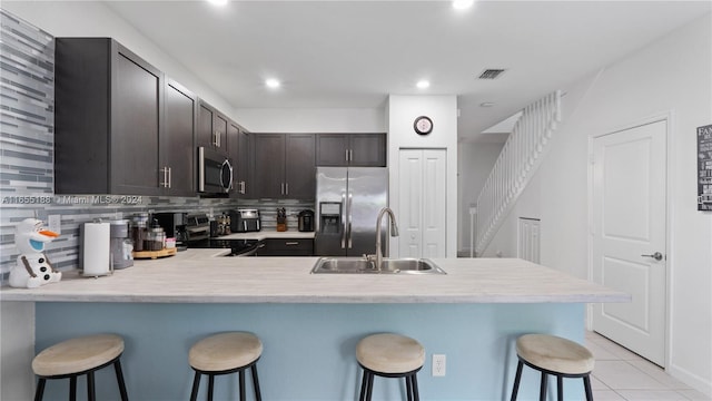 kitchen with a breakfast bar, sink, kitchen peninsula, stainless steel appliances, and dark brown cabinetry