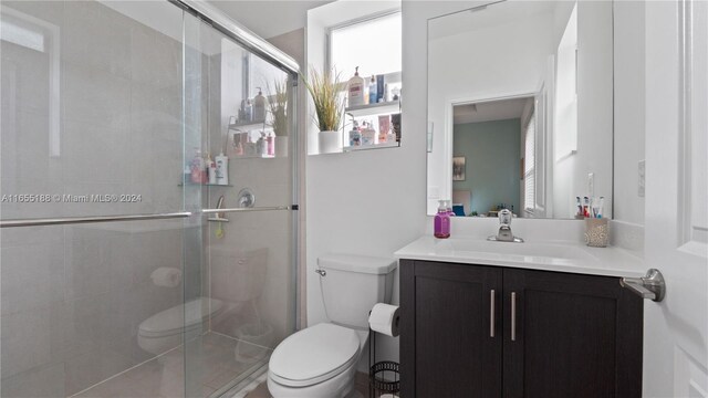 bathroom with a shower with door, vanity, and toilet