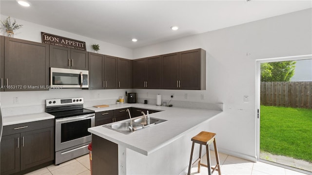 kitchen with appliances with stainless steel finishes, a kitchen breakfast bar, kitchen peninsula, dark brown cabinetry, and sink