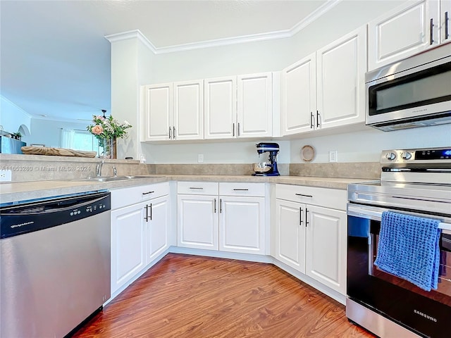 kitchen with stainless steel appliances, ornamental molding, white cabinetry, and light hardwood / wood-style floors