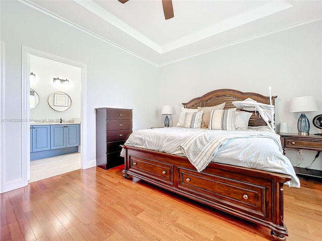 bedroom featuring crown molding, light hardwood / wood-style flooring, ensuite bath, ceiling fan, and a tray ceiling