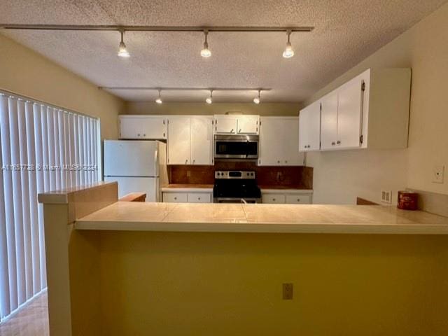 kitchen featuring track lighting, kitchen peninsula, a textured ceiling, appliances with stainless steel finishes, and white cabinetry