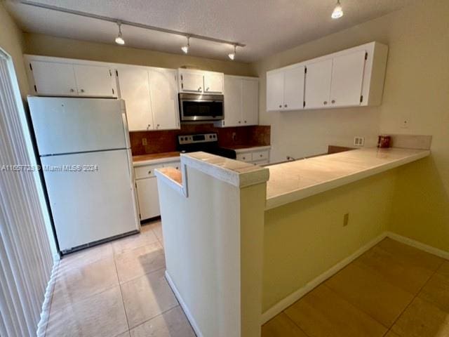 kitchen with kitchen peninsula, white refrigerator, white cabinetry, and range with electric cooktop