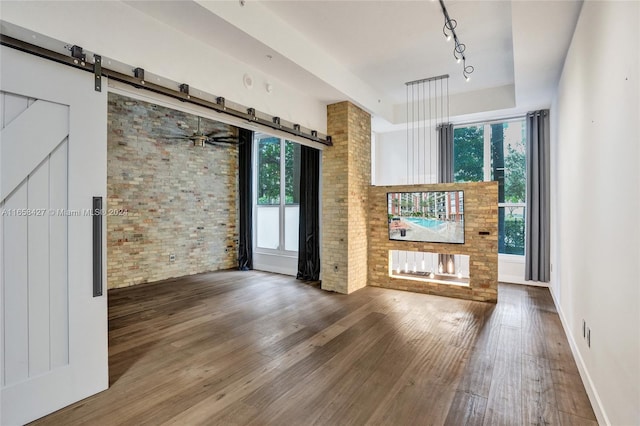 interior space featuring rail lighting, ceiling fan, dark wood-type flooring, brick wall, and a barn door