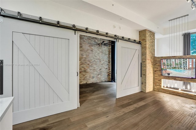 interior space featuring brick wall, hardwood / wood-style floors, ceiling fan, and a barn door