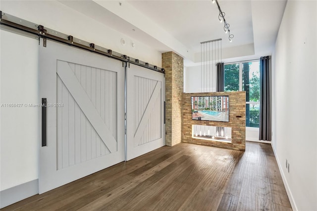 interior space featuring a barn door, rail lighting, hardwood / wood-style flooring, and brick wall