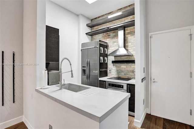 kitchen featuring appliances with stainless steel finishes, wall chimney exhaust hood, hardwood / wood-style flooring, and kitchen peninsula