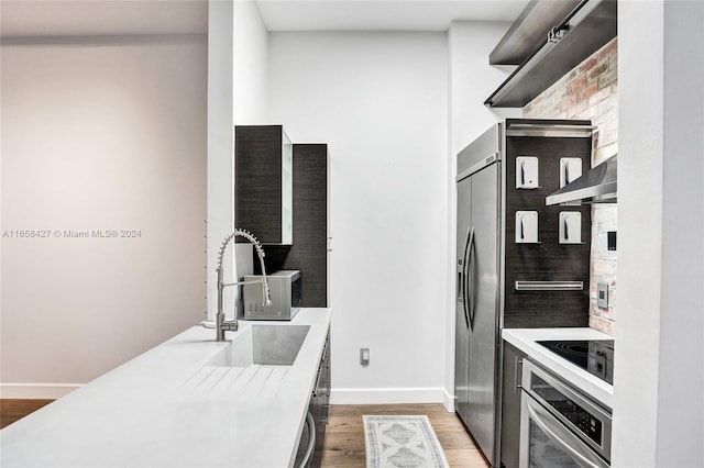 kitchen with wall chimney exhaust hood, appliances with stainless steel finishes, hardwood / wood-style floors, and sink