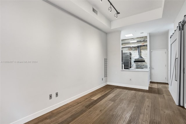 unfurnished bedroom with a barn door, rail lighting, and wood-type flooring