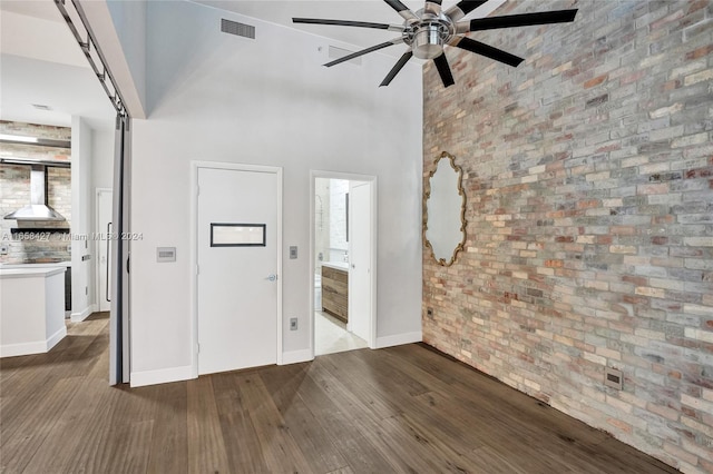 unfurnished living room with a towering ceiling, ceiling fan, hardwood / wood-style flooring, and brick wall