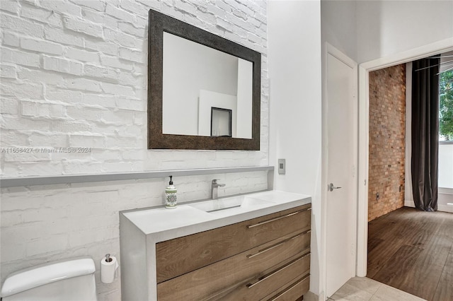 bathroom with brick wall, toilet, vanity, and wood-type flooring