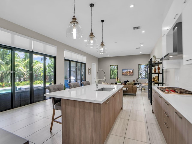 kitchen featuring a large island, ventilation hood, sink, stainless steel gas cooktop, and hanging light fixtures