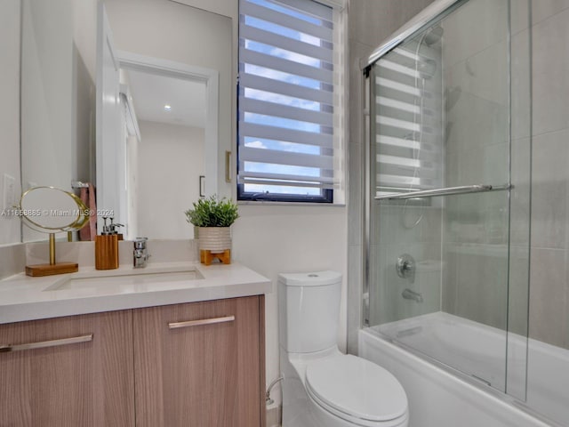 full bathroom featuring shower / bath combination with glass door, vanity, toilet, and a wealth of natural light