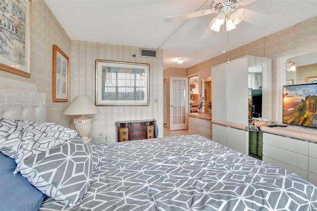 bedroom with wallpapered walls, visible vents, and a textured ceiling