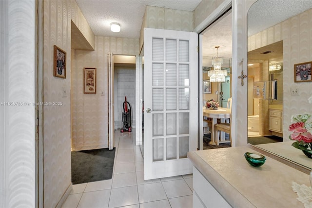 bathroom featuring wallpapered walls, a notable chandelier, tile patterned flooring, and a textured ceiling