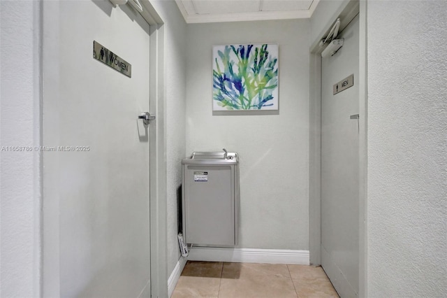 hallway with light tile patterned floors, baseboards, and crown molding