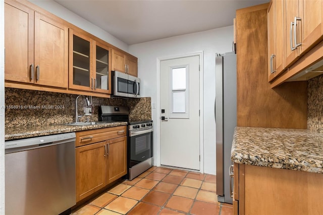 kitchen with backsplash, light tile patterned floors, appliances with stainless steel finishes, sink, and dark stone counters