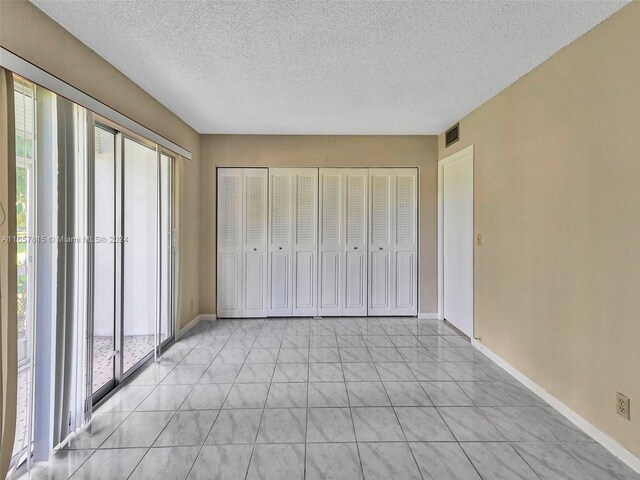 unfurnished bedroom featuring multiple windows, light tile patterned floors, and a textured ceiling