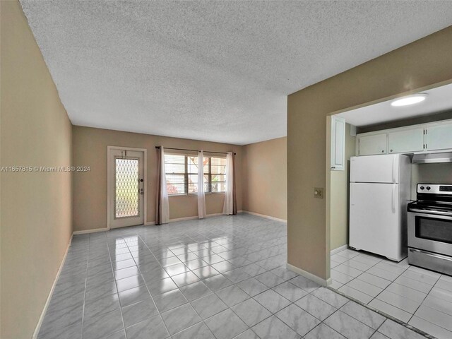 kitchen with white refrigerator, white cabinetry, light tile patterned flooring, stainless steel range with electric cooktop, and a textured ceiling