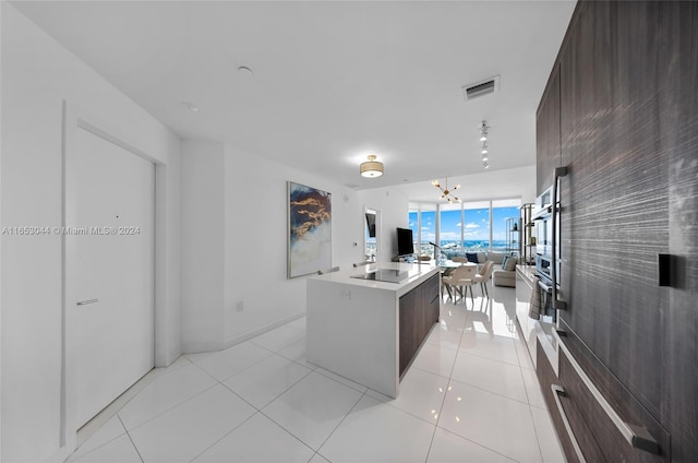 kitchen with an island with sink, light tile patterned flooring, a chandelier, oven, and black electric stovetop