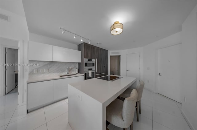 kitchen with white cabinetry, tasteful backsplash, a breakfast bar, a center island with sink, and sink