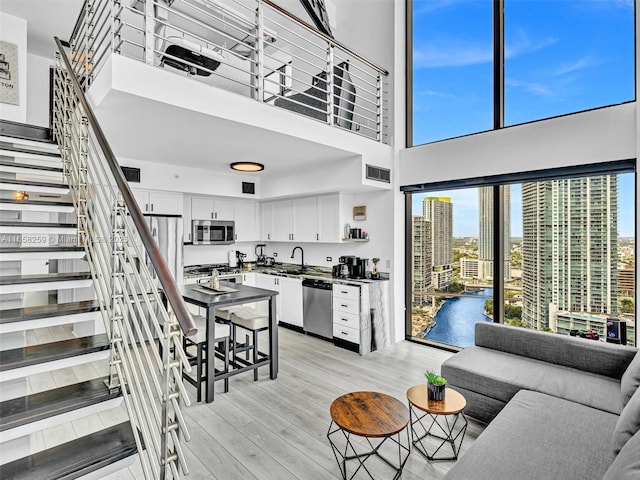 living room with a view of city, visible vents, stairway, a high ceiling, and light wood-type flooring