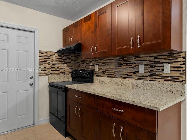 kitchen featuring tasteful backsplash, light stone counters, light tile patterned floors, black range with electric stovetop, and range hood