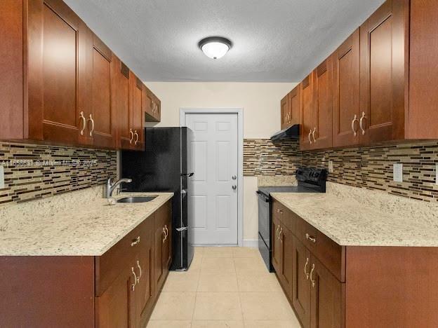 kitchen featuring black / electric stove, sink, light tile patterned floors, tasteful backsplash, and extractor fan