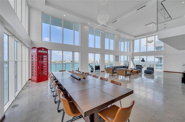 dining space with a water view, a healthy amount of sunlight, a towering ceiling, and a chandelier