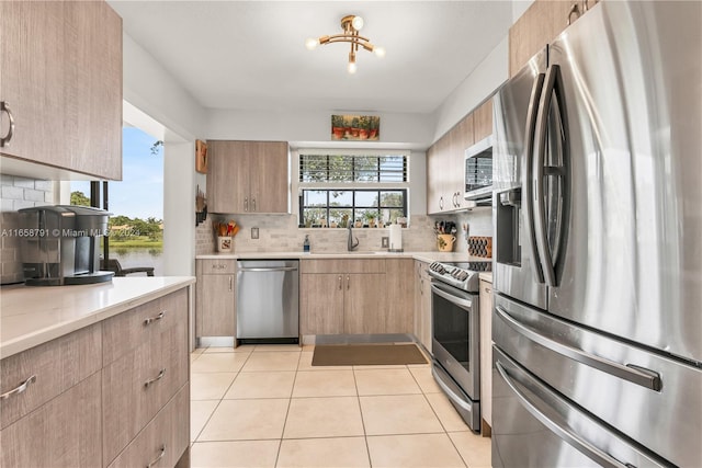 kitchen with light tile patterned flooring, sink, backsplash, stainless steel appliances, and an inviting chandelier