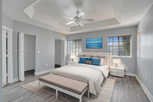 bedroom with a tray ceiling, light hardwood / wood-style flooring, and ceiling fan