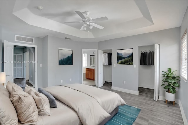 bedroom featuring a tray ceiling, light wood-type flooring, ensuite bathroom, and ceiling fan