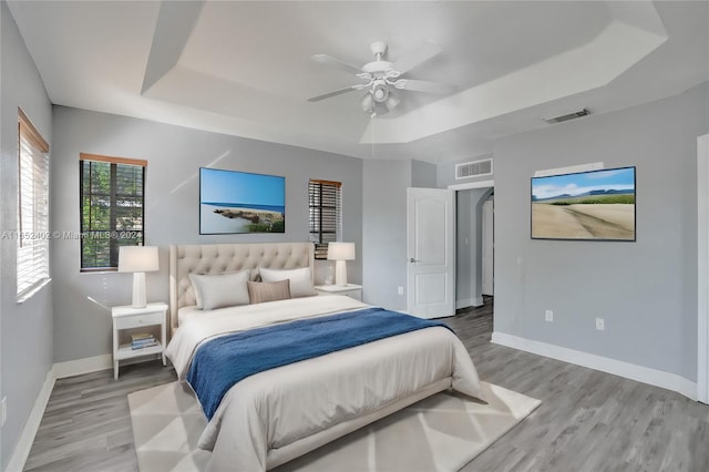 bedroom with ceiling fan, wood-type flooring, and a tray ceiling