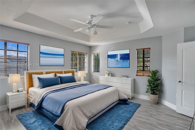 bedroom with multiple windows, ceiling fan, a raised ceiling, and light hardwood / wood-style floors