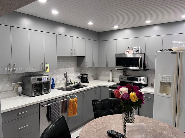 kitchen with gray cabinetry, decorative backsplash, sink, and stainless steel appliances