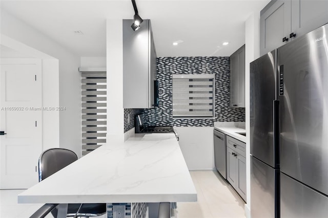 kitchen with gray cabinetry, appliances with stainless steel finishes, decorative backsplash, and light stone countertops