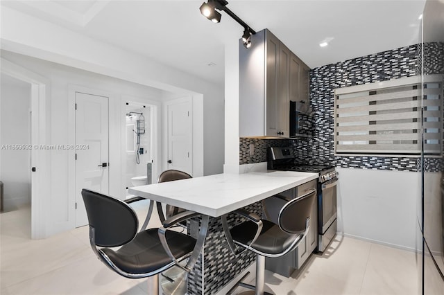 kitchen with light tile patterned floors, decorative backsplash, and stainless steel range with electric stovetop