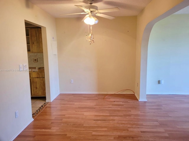 unfurnished room featuring light wood-type flooring, baseboards, arched walkways, and a ceiling fan