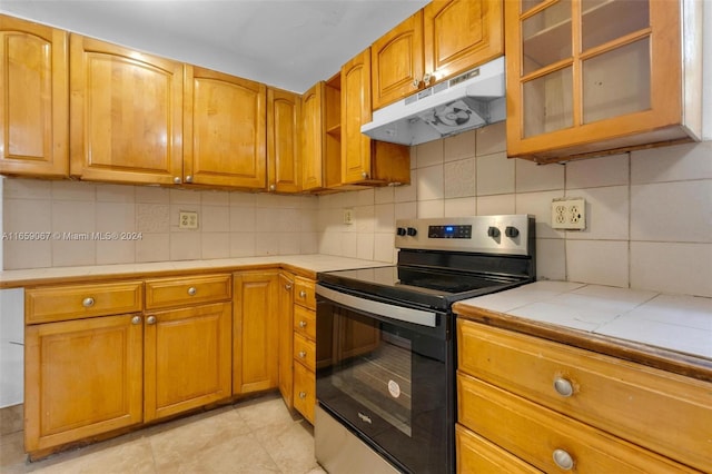 kitchen with tile countertops, tasteful backsplash, stainless steel electric stove, and light tile patterned floors