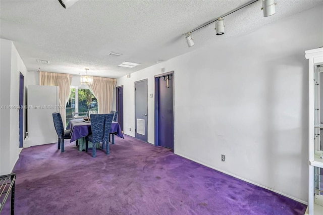 carpeted dining room featuring a textured ceiling, rail lighting, and an inviting chandelier