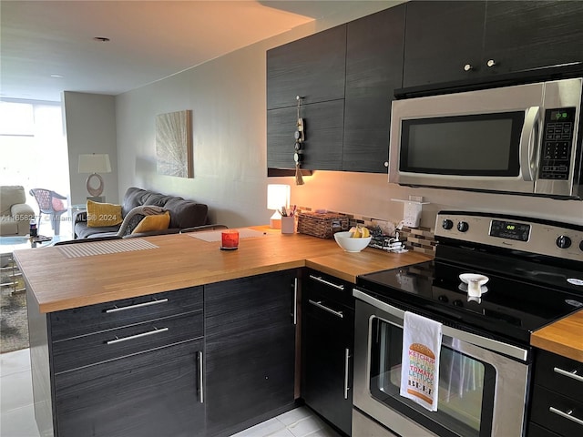 kitchen featuring light tile patterned floors, wooden counters, kitchen peninsula, and stainless steel appliances