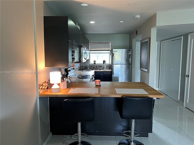 kitchen with stainless steel appliances, a kitchen breakfast bar, butcher block counters, and kitchen peninsula