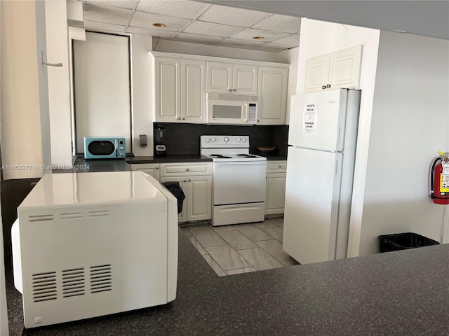 kitchen with white appliances, a drop ceiling, and white cabinetry