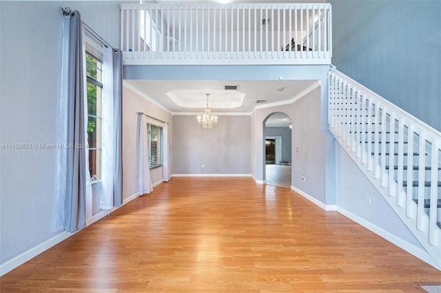 interior space featuring light wood-type flooring, a raised ceiling, crown molding, and a notable chandelier